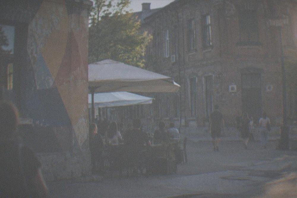 A street corner with a painted wall, outdoor cafe tables and people passing by