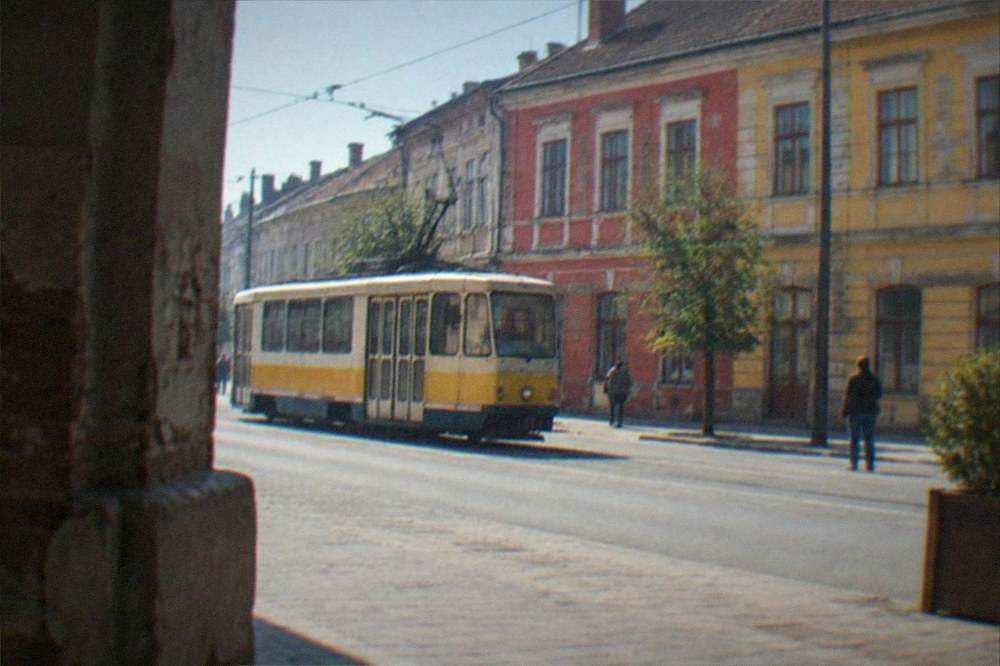 A tram passing a building with colorful graffiti on a city street in late afternoon light
