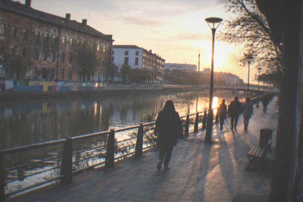 A wide view of a city promenade beside a canal with painted walls and people strolling at sunset