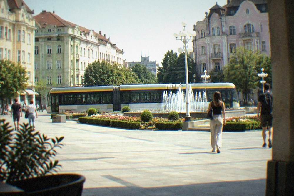 A modern tram crossing a city square in front of pastel-colored buildings