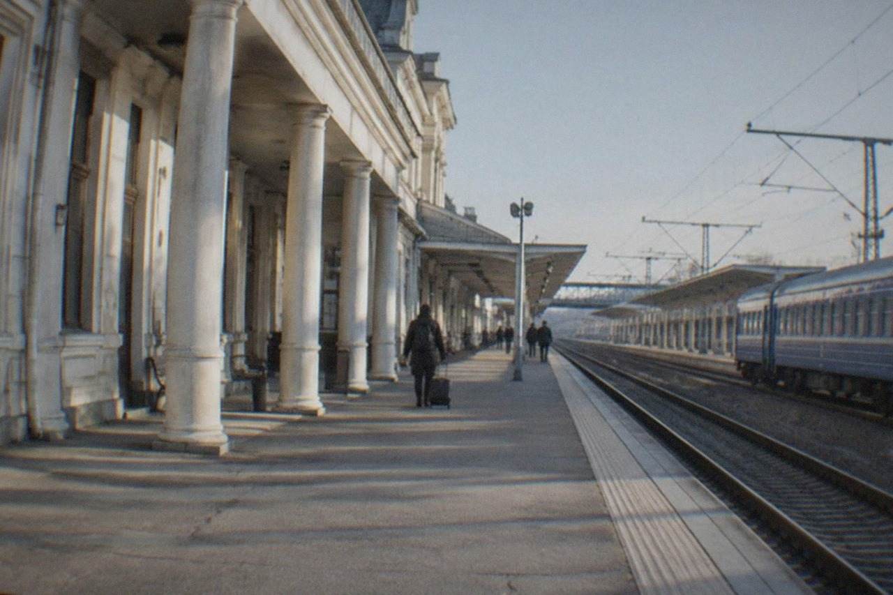 The station building and platforms of Timisoara Nord under a clear sky, with a blue passenger train waiting at the platform
