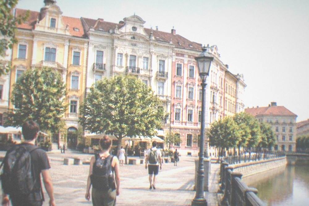 Travelers with backpacks walking across a square in central Timisoara past colorful facades