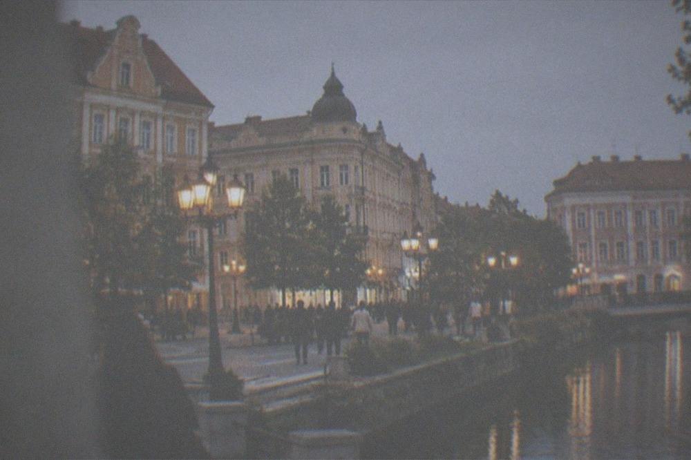 An evening view of a lit square in central Timisoara with people strolling under the lights