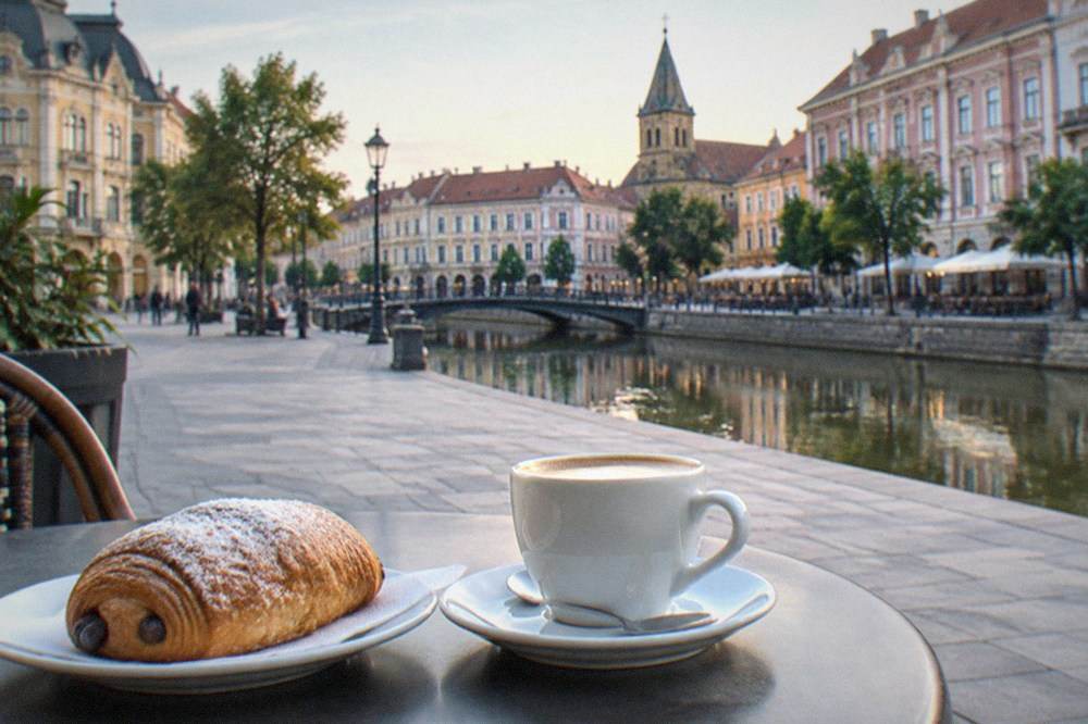 A coffee and a pastry on a cafe table beside a sunlit square