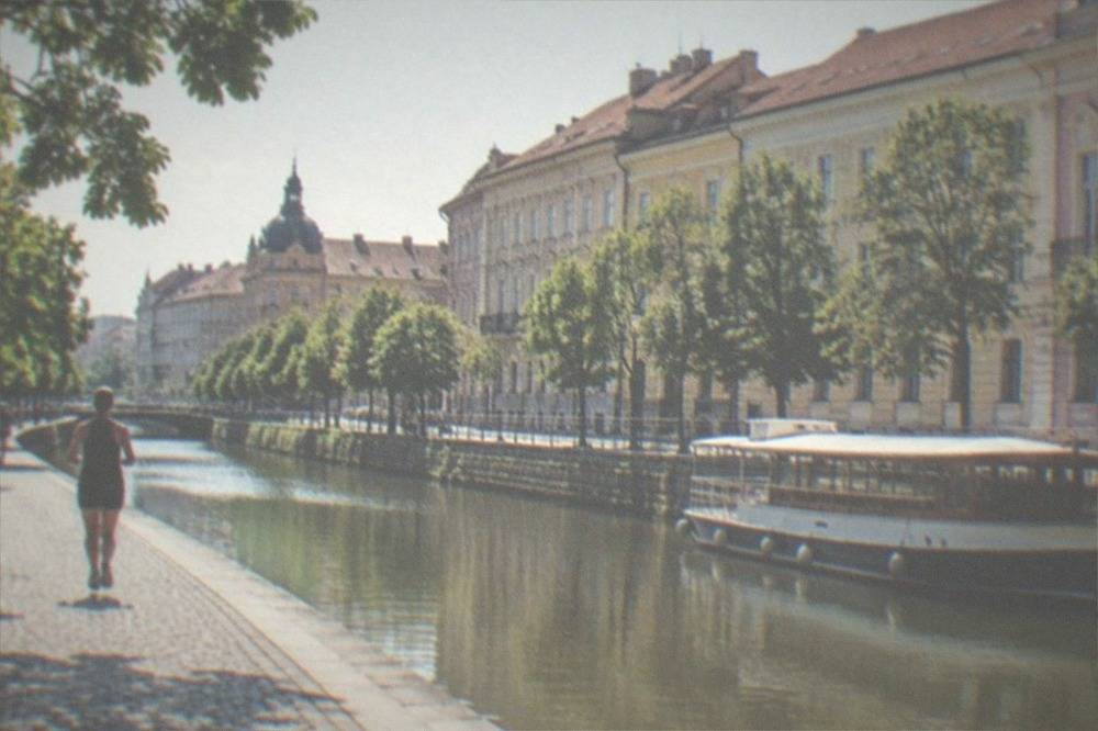 A river boat moored on a city canal with tree-lined banks and old buildings behind