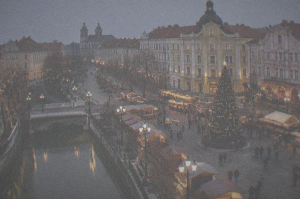 An illuminated city square at night with a lit Christmas tree and market stalls