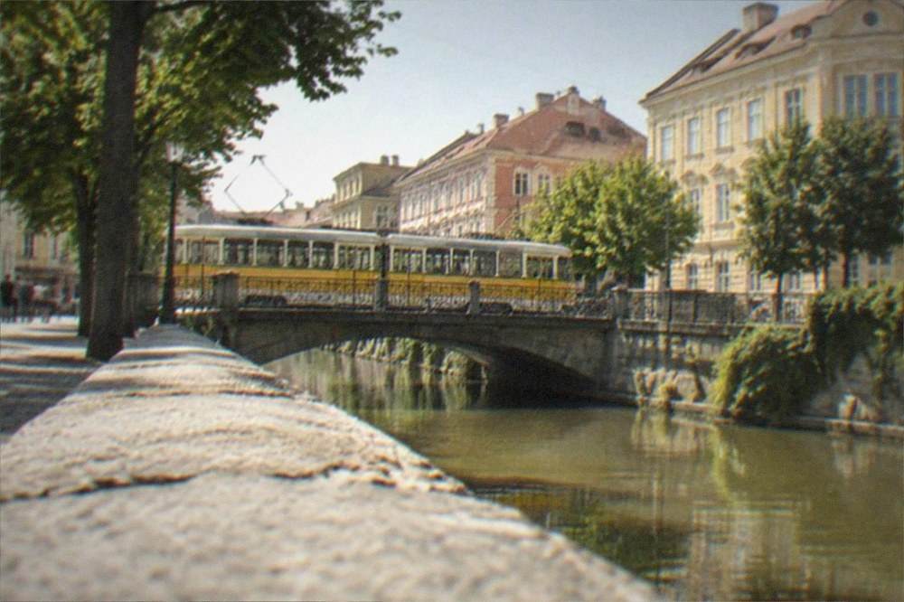 A yellow tram crossing a bridge over a city canal lined with trees