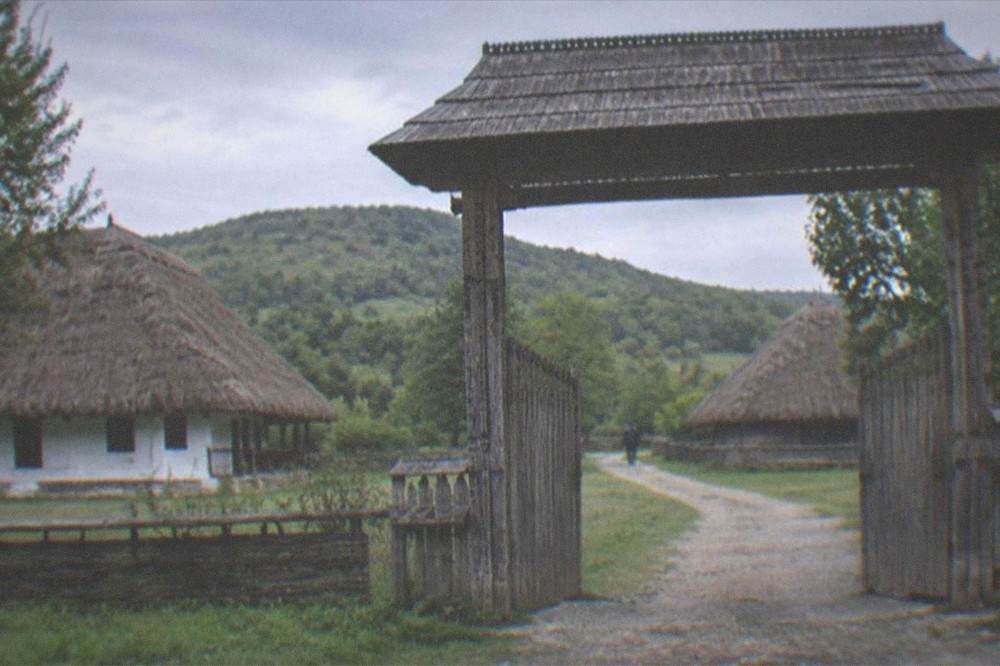 A wooden village gate and green hills at an open-air museum near Timisoara