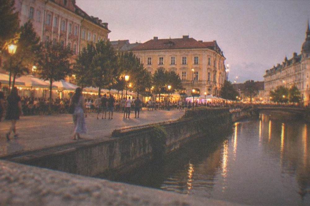 An illuminated city square at night with people walking between lit cafes