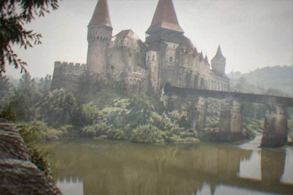 A Gothic castle with tall towers reflected in water at Corvin Castle