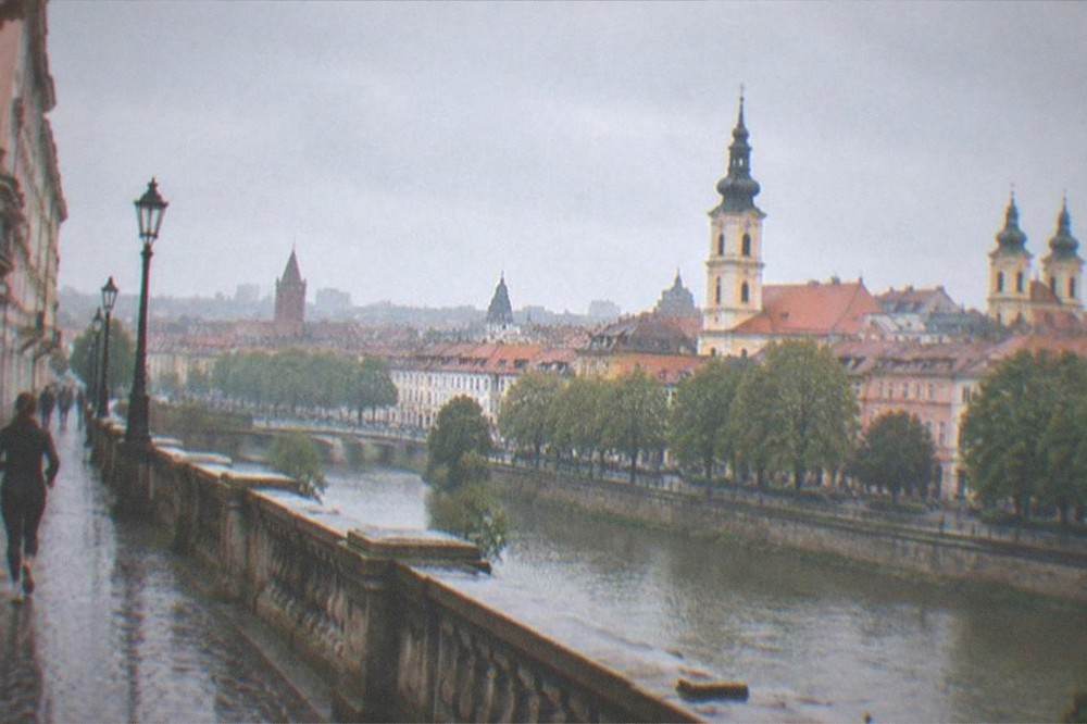 A panoramic view over red rooftops and church towers toward a river