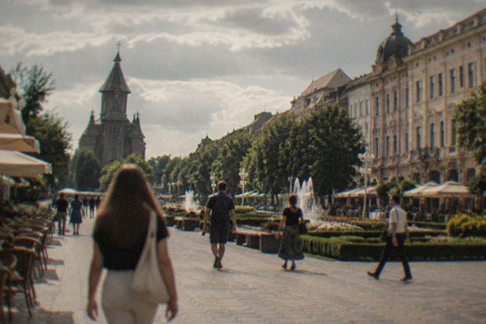 Pedestrians crossing a baroque square with pastel buildings and outdoor cafe tables