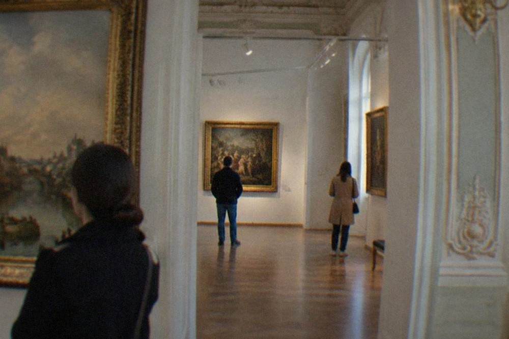 Visitors viewing paintings inside a brightly lit baroque art museum gallery
