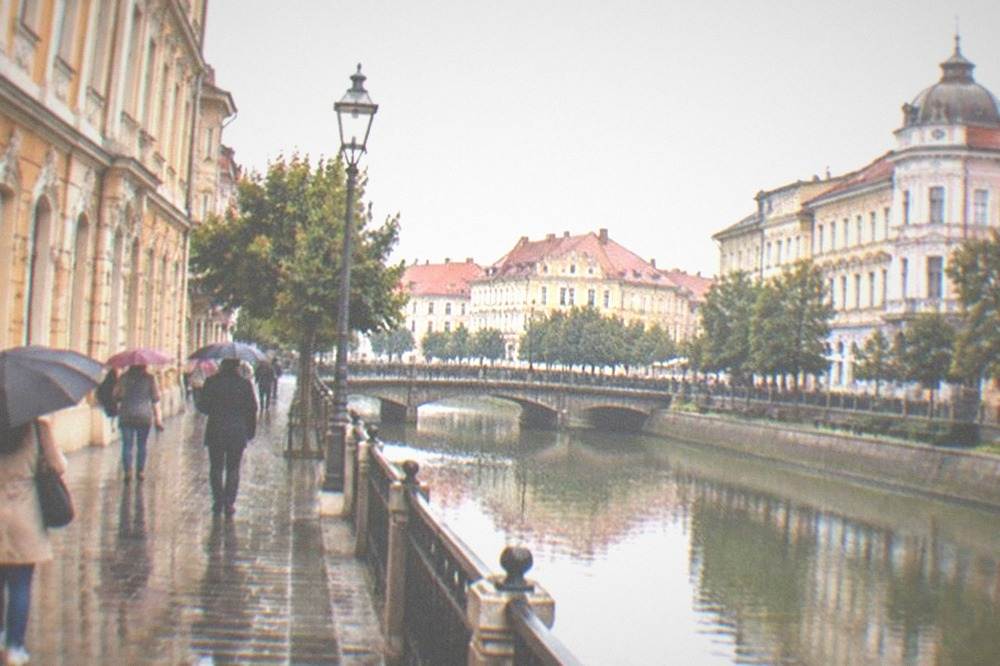 People walking with umbrellas past colorful facades on a wet city street